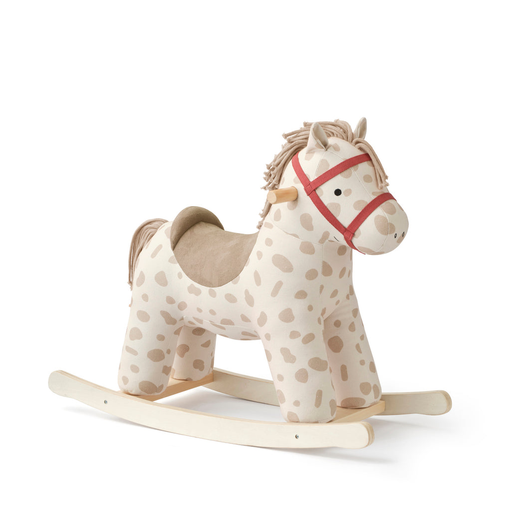 Soft-spotted rocking horse with a beige polka dot body, red harness, and wooden rockers, conveying a playful and cozy feel for children.