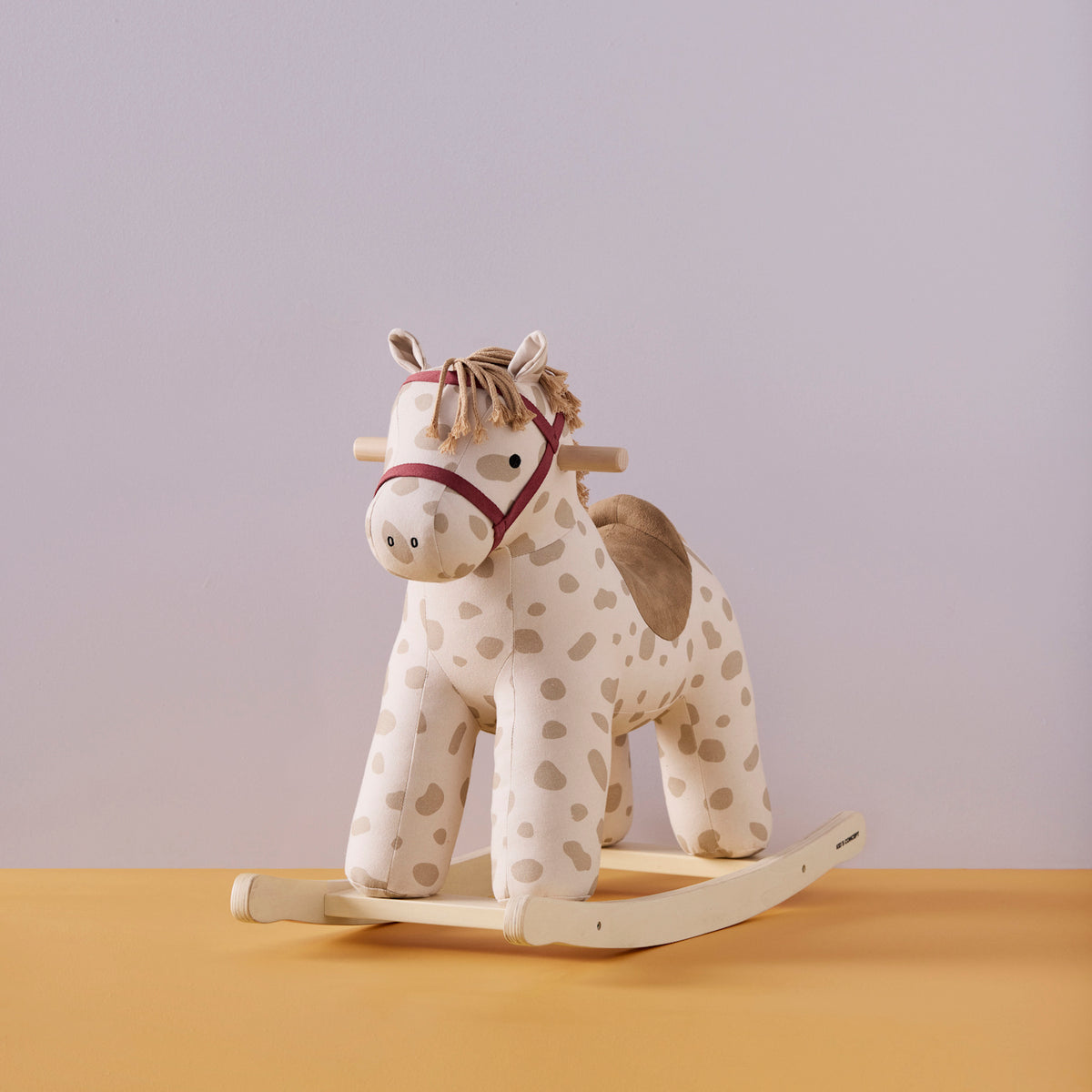 Plush spotted rocking horse toy with a wooden base, fabric saddle, and reins.