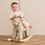 Toddler sitting on a striped plush rocking horse in a light-toned room.