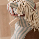 Close-up view of the yarn mane and wooden handlebar of a striped plush rocking horse.