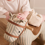 Close-up of a toddler riding a striped fabric rocking horse toy and leaning forward.