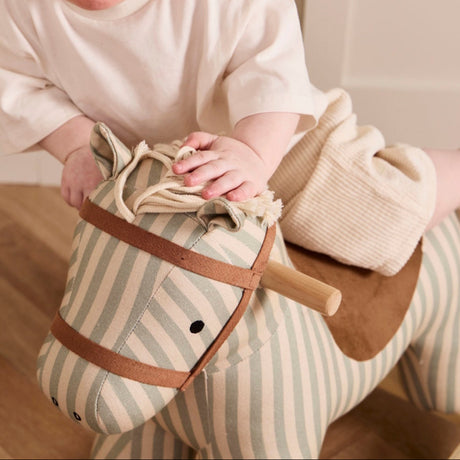Close-up of a toddler riding a striped fabric rocking horse toy and leaning forward.