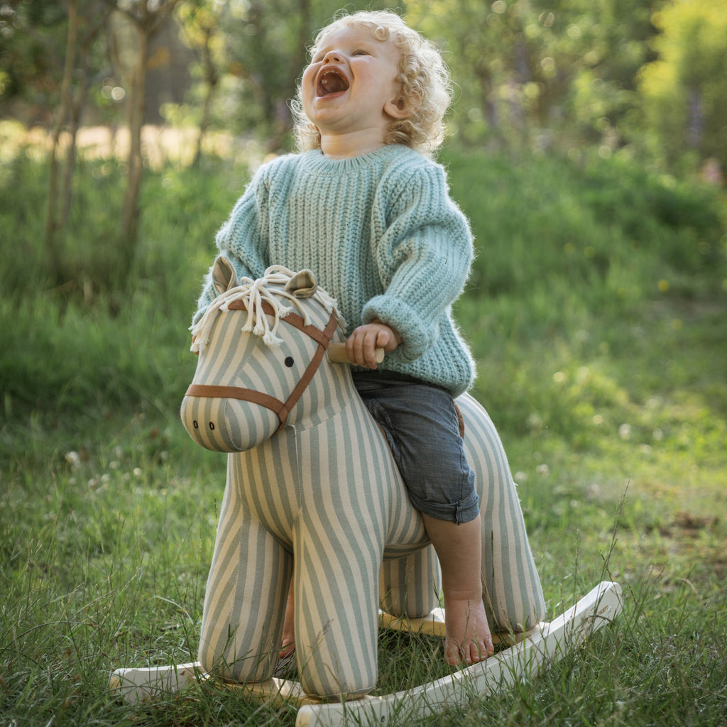 Soft, striped rocking horse with a beige and blue pattern, wooden rockers, and a plush brown saddle. It evokes a playful, nostalgic feel.