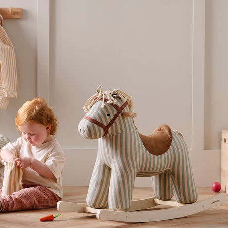 Red-haired toddler playing on the floor next to a striped plush rocking horse toy.