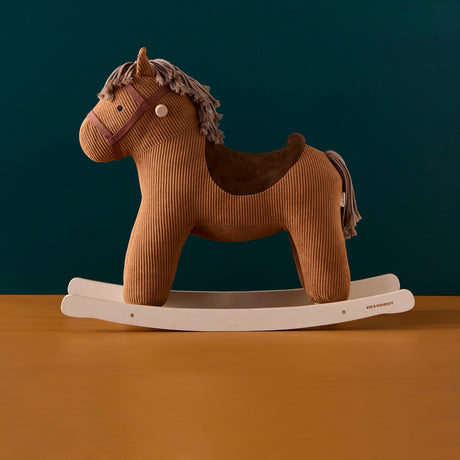 Brown corduroy plush rocking horse on wooden rockers against a dark teal wall and tan floor.