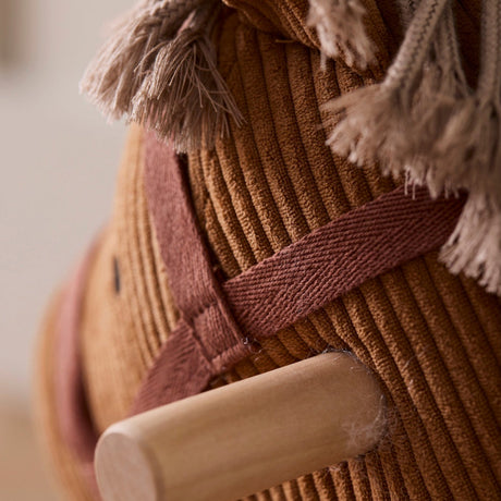 Close-up of a brown corduroy rocking horse head with a fringe mane and wooden handle grip.