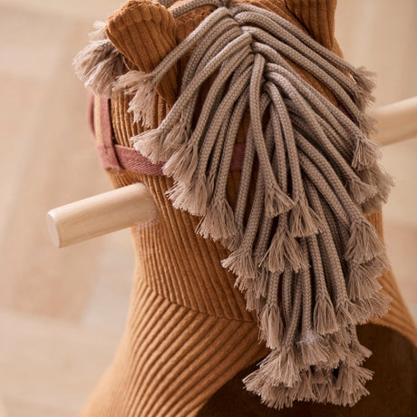 Close-up of a brown corduroy rocking horse showing its braided yarn mane and wooden handles.
