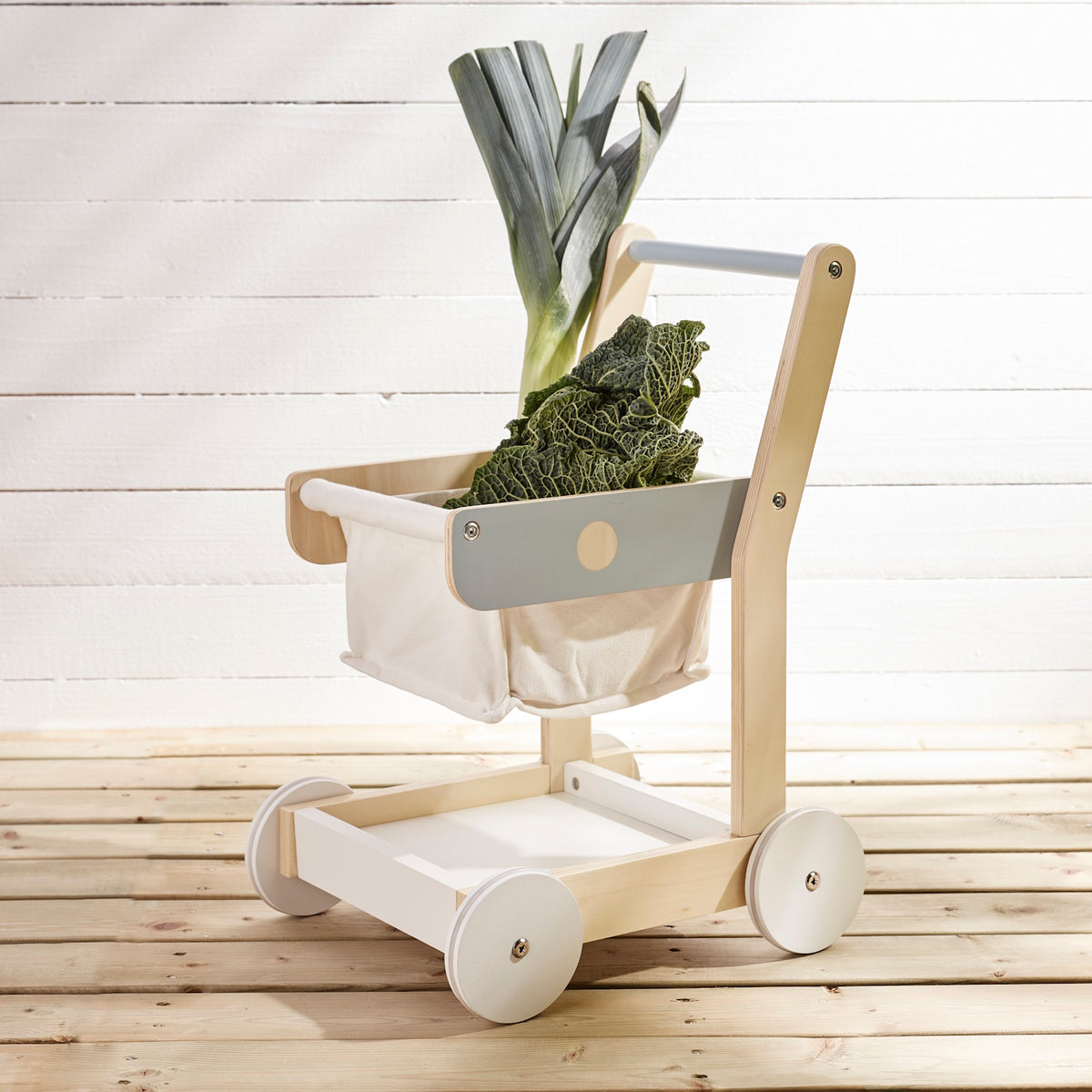Wooden toy shopping trolley with fresh leek and kale in its fabric basket.