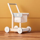 Wooden toy shopping trolley with a fabric basket set against a yellow wall and wood floor.