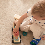 Child playing with a wooden sorting ring toy truck on a carpeted floor.