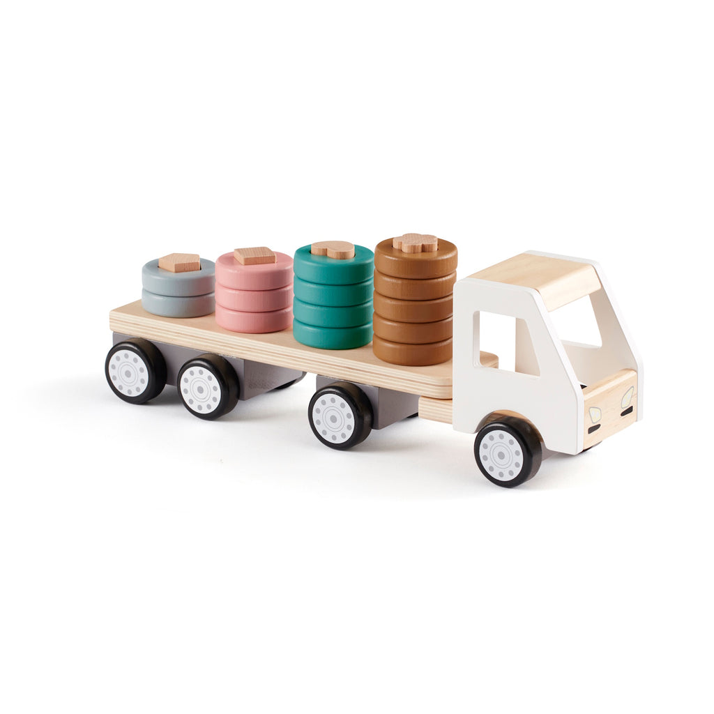 A wooden toy truck with a white cab and black wheels. The flatbed carries cylindrical wooden stacks in gray, pink, teal, and brown, creating a playful and organized look.