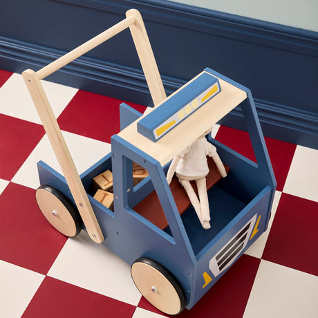 High-angle view of a blue wooden toy walker truck carrying a ragdoll and blocks on a checkered floor.