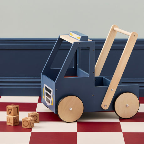 Empty blue wooden toy walker truck next to wooden alphabet blocks on a checkered floor.