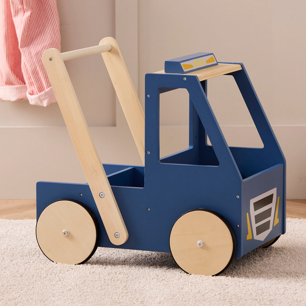 Blue wooden toy walker truck with natural wood wheels and handle resting on a plush beige rug.