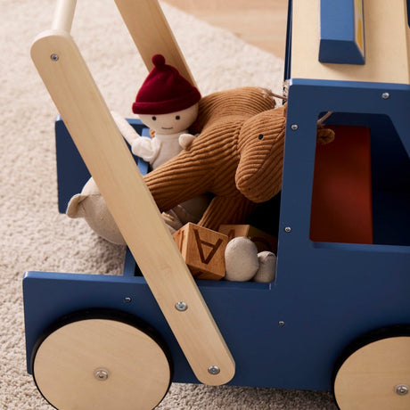 Side view of a blue wooden toy walker truck filled with plush toys and wooden alphabet blocks.
