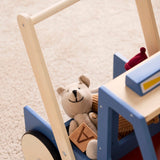 Close-up view of a blue wooden toy walker truck with a stuffed teddy bear and wooden blocks inside.