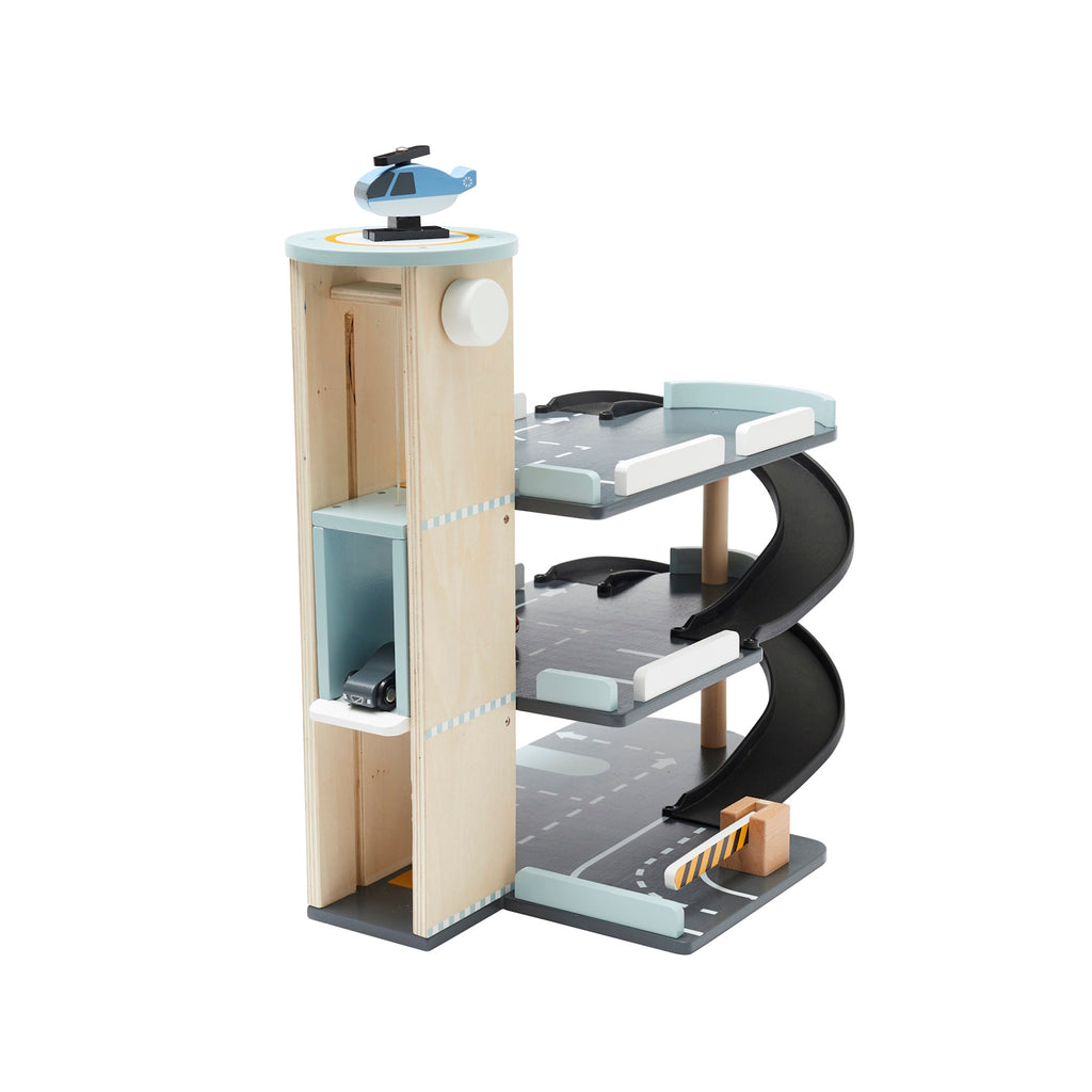Wooden toy parking garage with three levels, spiral ramp, three toy cars, a helicopter on the rooftop helipad, and a traffic barrier for pretend play.