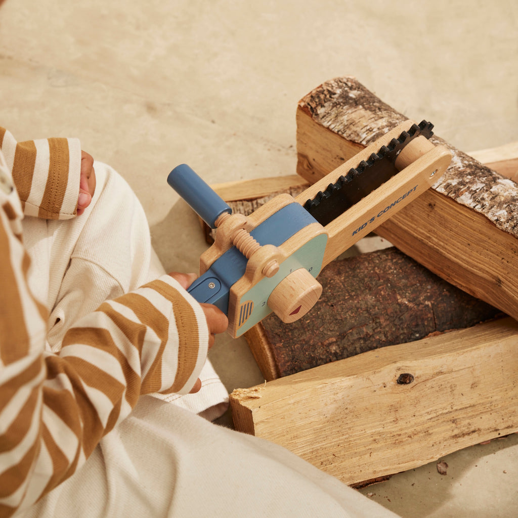Wooden toy chainsaw with blue handle and details, featuring a rotating knob and black ridged edge. "Kid’s Concept" is printed on the side.