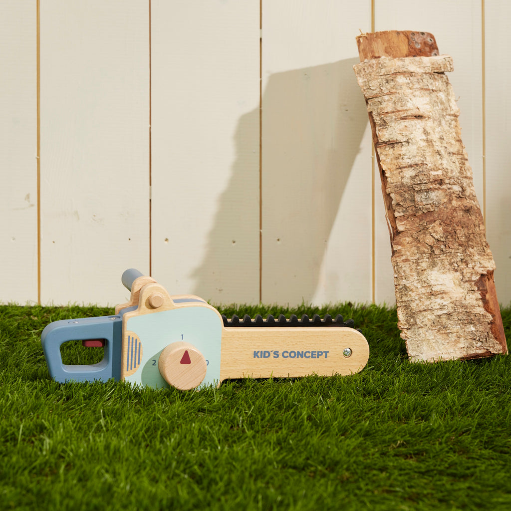 Wooden toy chainsaw with blue handle and details, featuring a rotating knob and black ridged edge. "Kid’s Concept" is printed on the side.