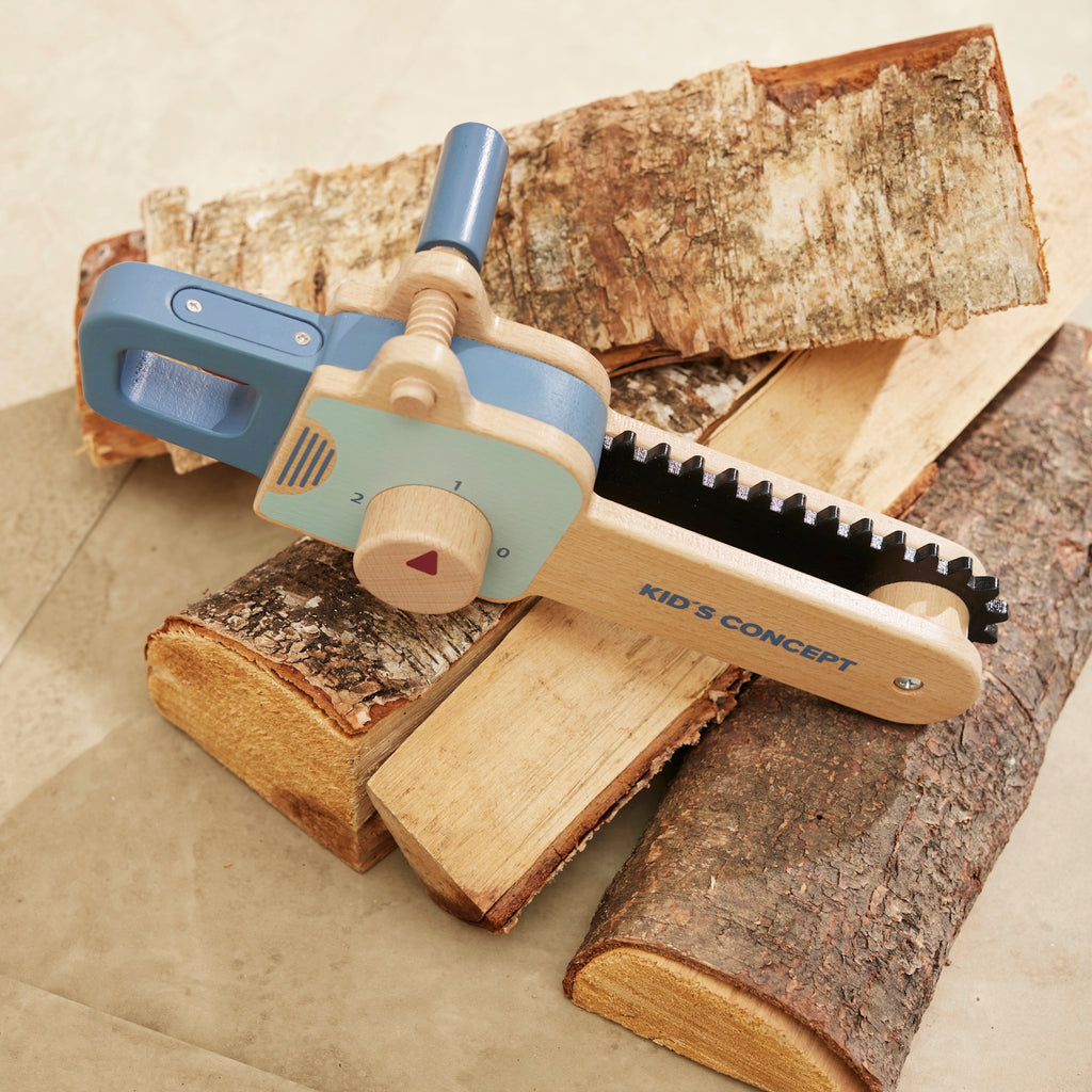Wooden toy chainsaw with blue handle and details, featuring a rotating knob and black ridged edge. "Kid’s Concept" is printed on the side.