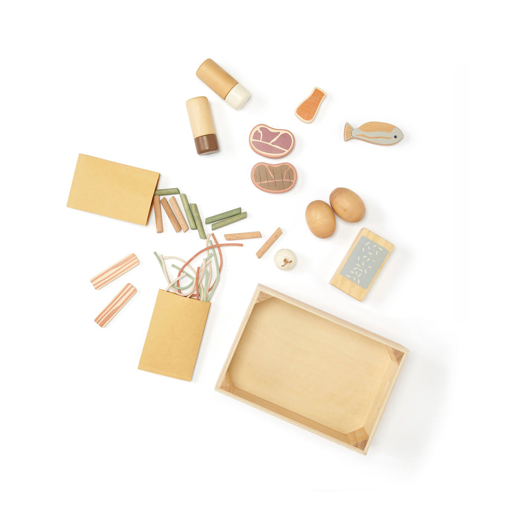 Assorted wooden toy food items are scattered, including eggs, fish, and pasta, alongside small wooden boxes. The tone is playful and educational.