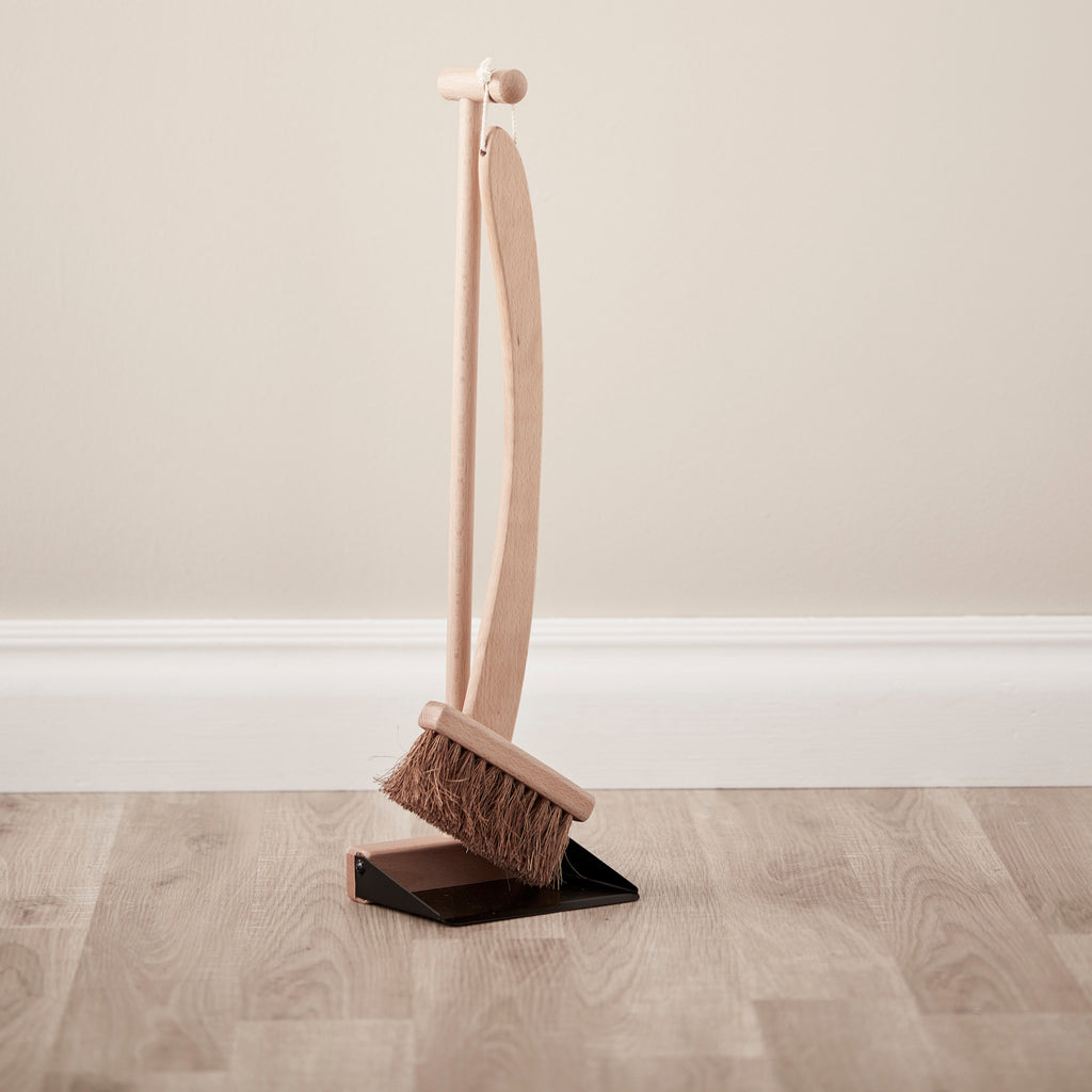 Wooden broom and dustpan set with a sleek, minimalist design. The broom features natural bristles and hangs from a matching stand, conveying simplicity.