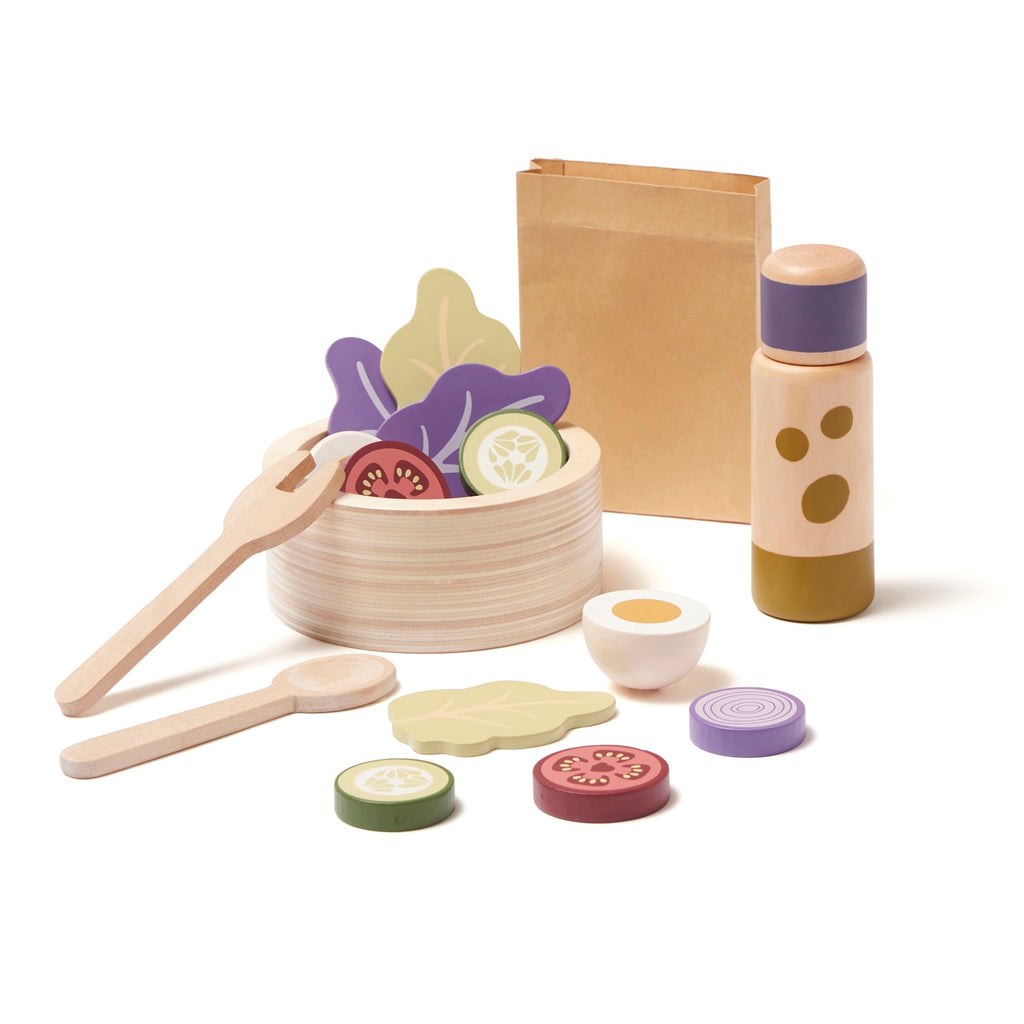 Wooden toy salad set with a bowl, utensils, slices of vegetables, and a bottle. Items are colorful, playful, and spread out, conveying a fun, culinary theme.