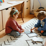 Two children sitting on a rug using a Kidydraw Mini tracing tablet for educational drawing and writing games.