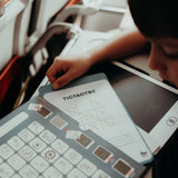 Child playing Tic-Tac-Toe on a portable travel activity board with educational game cards during a flight.