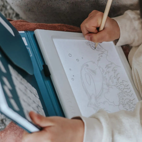 A child drawing an underwater scene with a fish using a pencil on an illuminated drawing pad.