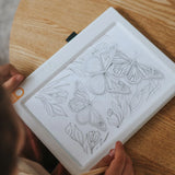 A child tracing butterfly and flower sketches on an illuminated white drawing pad.