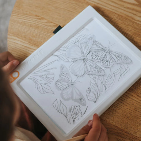 A child tracing butterfly and flower sketches on an illuminated white drawing pad.