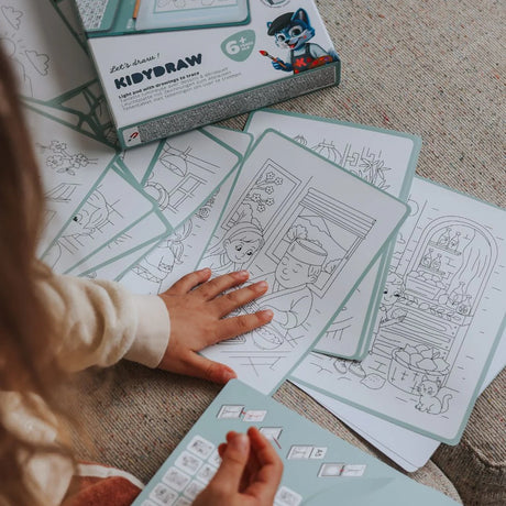 A child sorting through black-and-white tracing sheets from a KIDYDRAW kit scattered on a couch.