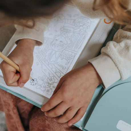 Child's hands tracing a line drawing of a fruit market on an illuminated Kidywolf drawing pad.