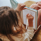An over-the-shoulder view of a child using a pencil to trace a drawing on an illuminated light pad.