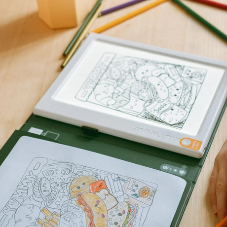 An illuminated drawing pad used to trace a food-themed cartoon illustration onto paper.
