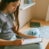 A girl sitting cross-legged draws with a pencil on an illuminated light-up sketching pad in her room.