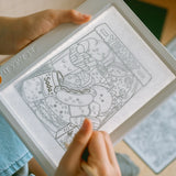 A child using a pencil to trace a cute food doodle illustration on an illuminated drawing pad.