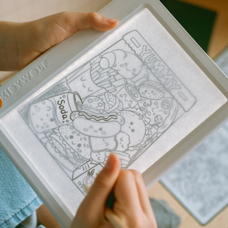 A child using a pencil to trace a cute food doodle illustration on an illuminated drawing pad.