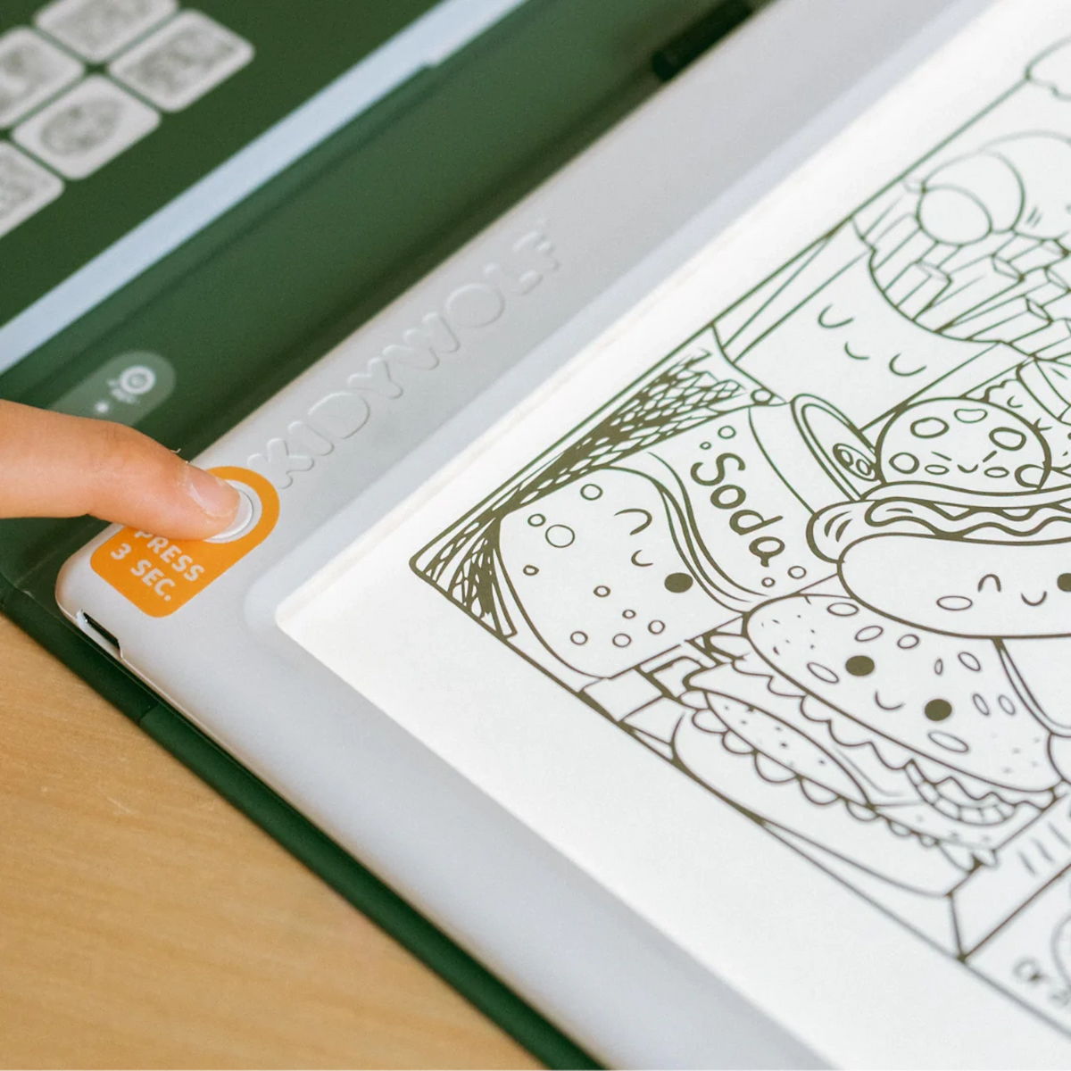 A finger presses the power button on an illuminated Kidywolf drawing pad featuring cartoon food illustrations.