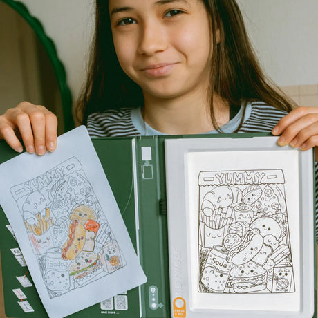 A girl holding an illuminated drawing pad next to her colored-in sketch of cartoon food.