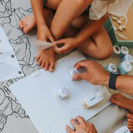 An adult and child building circuits together with a toy electrical kit on a world map play mat.