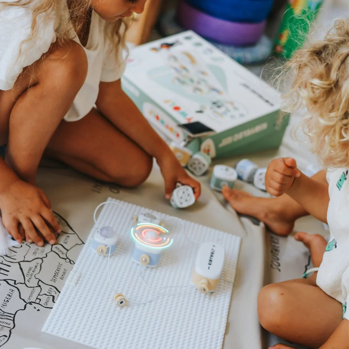 Two children playing on the floor with a toy electronics kit featuring a spinning, glowing fan component.
