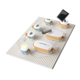 An educational toy electronics kit assembled on a building plate with a hand crank, solar panel, and lit bulb.