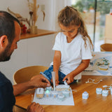 A young girl and a man build an electronics toy kit together at a wooden table.