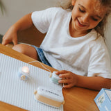 A smiling child plays with an electronic starter kit, lighting up a small bulb on a building grid.