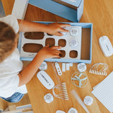 A child unboxing an electrical kit toy starter pack on a wooden table.
