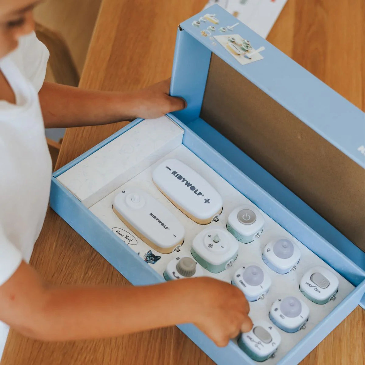 A child opens a Kidywolf electronics starter kit box filled with various modular components.