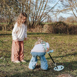 Two children using a toy metal detector and digging in a grassy field on a sunny day.