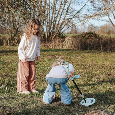 Two children using a toy metal detector and digging in a grassy field on a sunny day.